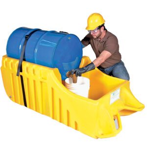 A worker in a hard hat and gloves uses the Vestil Drum Truck Dispensing & Containment Unit to handle a blue drum on a yellow spill containment pallet, pouring liquid into a white bucket while kneeling.