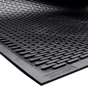 A close-up of the black MH-USA 3 x 5 Scraper Entry Mat shows raised horizontal lines with a textured design. The edge is slightly lifted, revealing its smooth underside.