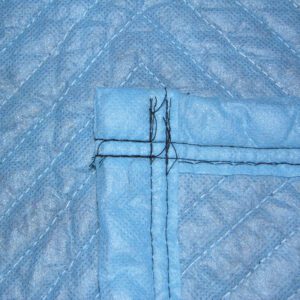 Close-up of a blue quilted fabric with black stitching in a cross pattern, similar to the durable texture of Vestil General Duty Moving Pads Cotton 12 Pack. The fabric looks textured, with evenly spaced parallel lines forming a geometric design.