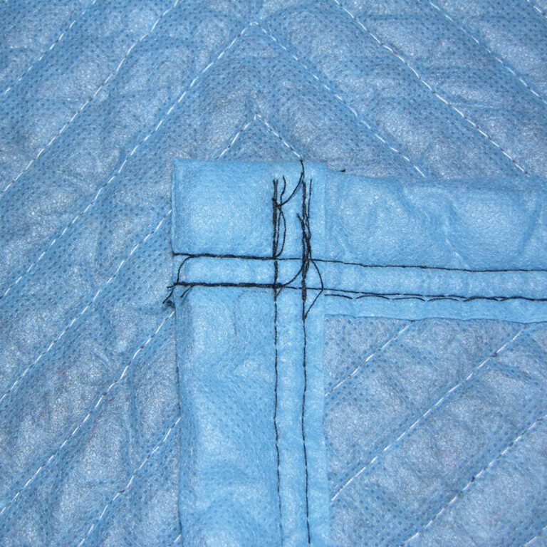 Close-up of a blue quilted fabric with black stitching in a cross pattern, similar to the durable texture of Vestil General Duty Moving Pads Cotton 12 Pack. The fabric looks textured, with evenly spaced parallel lines forming a geometric design.