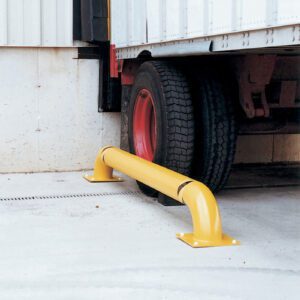 A Vestil Wheel Alignment Curb 144 In Yellow is positioned in front of a parked trucks rear wheels near a light-colored building, preventing backward movement and complementing the black tires with red rims.