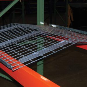 The Vestil Pallet Rack-Crown Wire Deck 52 X 42 In is set on orange beams and a green rack, forming a sturdy platform for items in the dim warehouse.