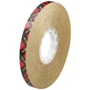 The 3M™ 924 Adhesive Transfer Tape, 1/2 x 11 yds. (6 Pack), features a brown adhesive surface with red and black plaid edging. It is shown on a white background, highlighting its thickness and central hole for easy mounting.