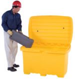Wearing a red hard hat, blue shirt, beige pants, safety goggles, and gloves, a person places a gray toolbox into an open-lid Vestil Utility Box - Yellow - No Wheels.