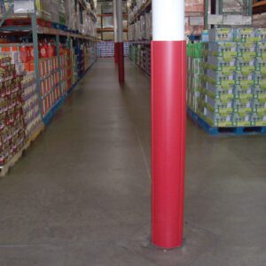 A warehouse aisle with shelves of packaged goods is centered by a Vestil Red Round Column Wrap 8 In, extending from floor to ceiling. The concrete floor stretches to the end of the aisle, enhancing visibility.