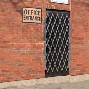 A brick wall with a sign reading Office Entrance above a Vestil Galvanized Scissor Gate-Expanded 75 In, featuring a diamond pattern. The gate stands out against the buildings red brick surface.