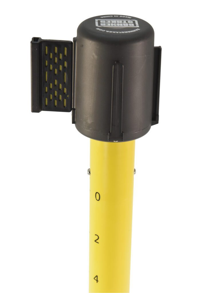 A black round electronic device, similar to the Vestil Web Barrier Caution Reel, Caution, is mounted on a yellow pole with 0 to 4 measurement markings and a flipped bracket on one side for enhanced cautionary functionality.