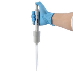A person wearing a blue glove holds a digital micropipette. The pipette is white with a digital display for precise liquid measurement and showcases a long, clear tip, reflecting the quality seen from top pipette tips suppliers.