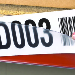 A person inserts a paper label with the code D003 and a barcode into a transparent holder on an orange shelf edge, enhancing warehouse designs by streamlining inventory management.