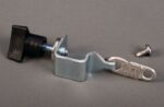 A metal clamp with a black plastic knob from the Justrite Dot Hold Down Replacement Kit rests on a gray surface, accompanied by a separate silver screw.