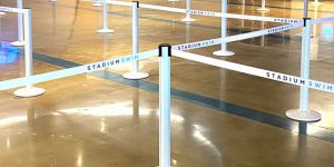 White heavy-duty crowd control barriers labeled Stadium Swim form a winding queue on a shiny, polished floor inside a spacious indoor area.
